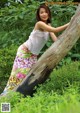 A woman leaning against a tree trunk in the woods.