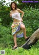 A woman in a white top and colorful skirt posing on a log.